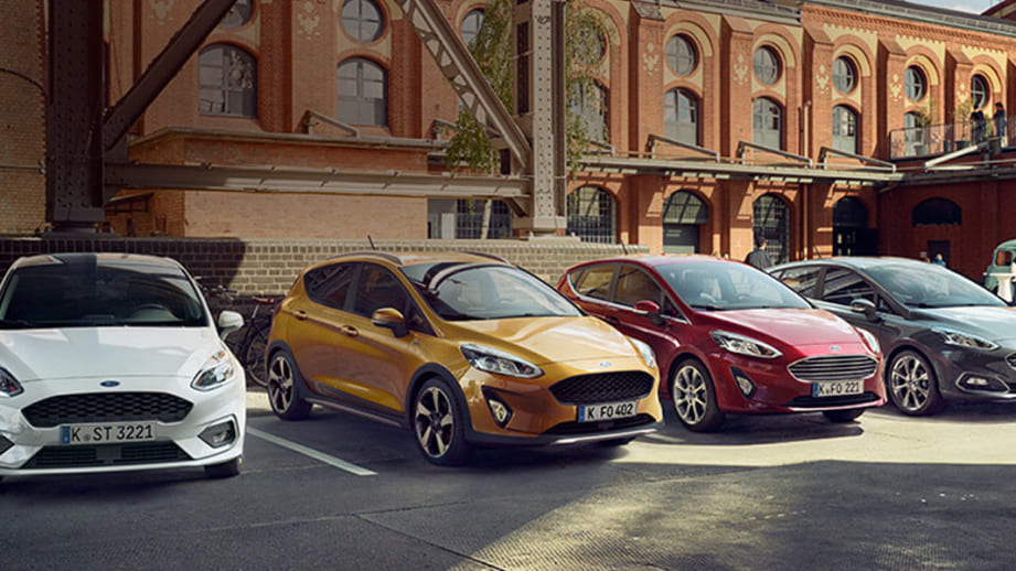 Mehrere Ford-Modelle parken vor einem alten Klinker-Gebäude